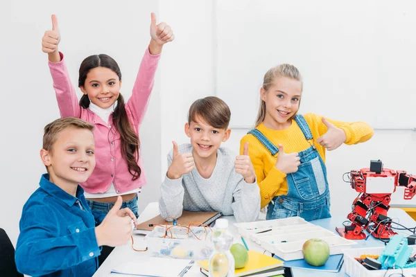 Cheerful schoolchildren looking at camera and showing thumbs up while having STEM lesson — Stock Photo