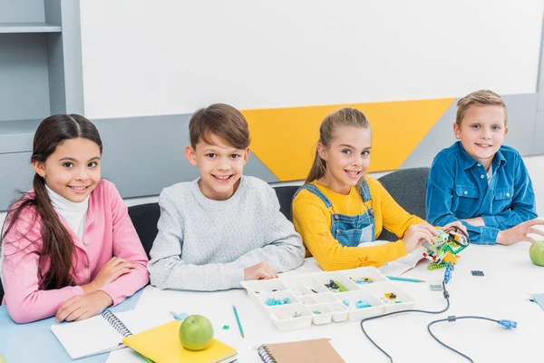 Happy classmates at desk looking at camera and working in STEM classroom — Stock Photo