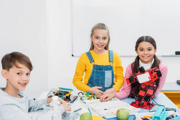 Glückliche Klassenkameraden am Schreibtisch, die in die Kamera schauen und im Klassenzimmer arbeiten — Stockfoto