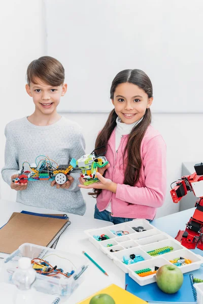 Glückliche Kinder schauen in die Kamera und präsentieren Robotermodelle bei der Vorlesung — Stockfoto