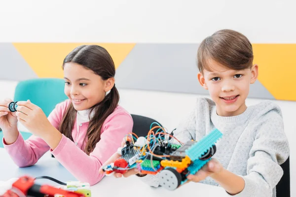Happy classmates holding robot model and working together on project during STEM lesson — Stock Photo