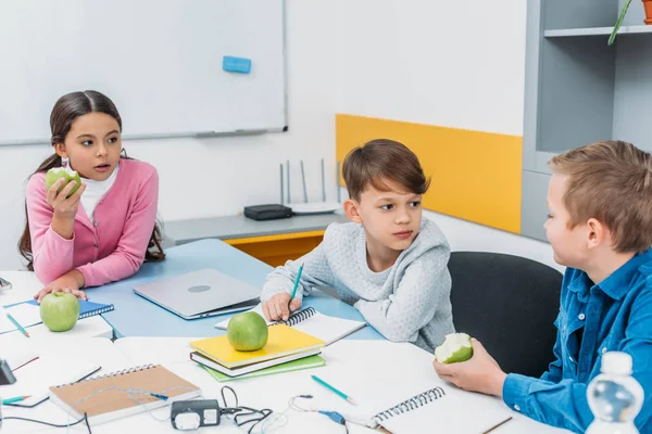 Camarades de classe assis à table, ayant pause, parler et manger des pommes en classe — Photo de stock