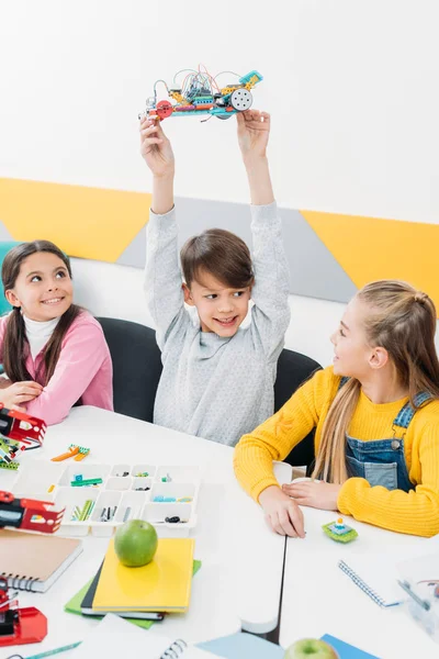 Feliz colegial presentando modelo robot mientras las colegialas lo miran durante la lección STEM - foto de stock