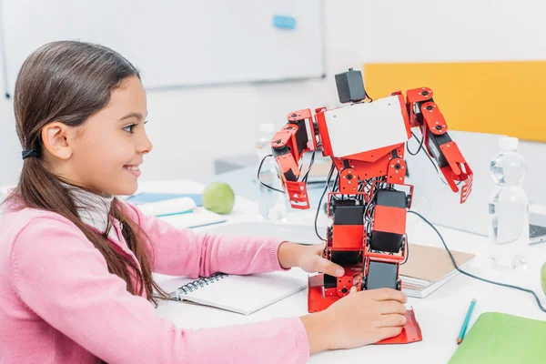 Adorável estudante sentada à mesa em sala de aula STEM e brincando com modelo de robô — Fotografia de Stock