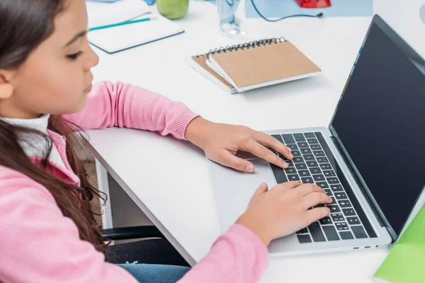 Colegiala sentado en el escritorio y el uso de la computadora portátil con pantalla en blanco durante la lección en el aula - foto de stock