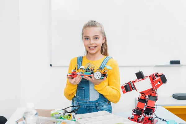 Улыбающаяся школьница смотрит в камеру и представляет модель робота ручной работы на уроке STEM — стоковое фото