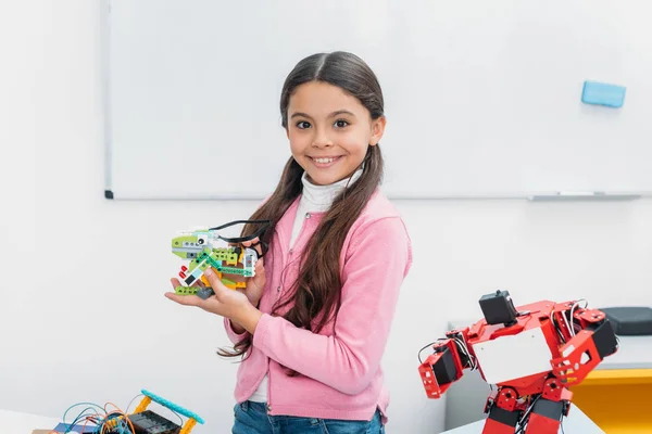 Усміхаючись школярка дивлячись на камеру і представляти ручної роботи робот модель в стовбурових урок — стокове фото