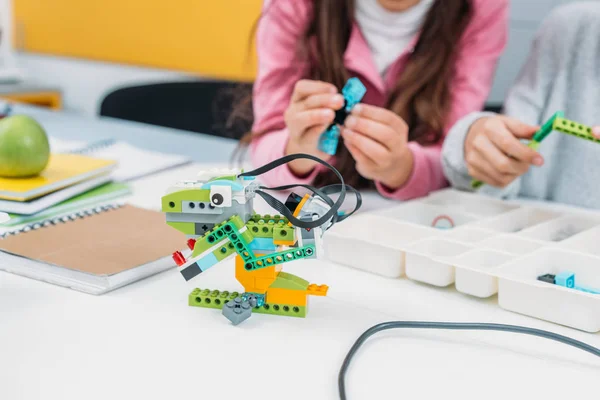 Visão recortada de colegas de classe trabalhando juntos no projeto durante a lição STEM com modelo de robô artesanal em primeiro plano — Fotografia de Stock