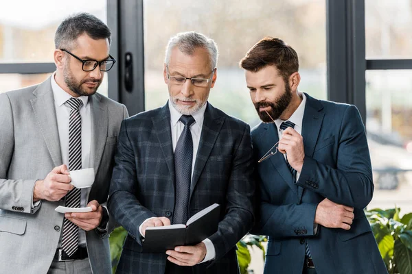 Professional businessmen in formal wear standing together and looking at notepad — Stock Photo