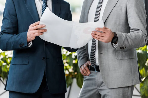 Cropped shot of businessmen holding paper with charts and working together in office — Stock Photo