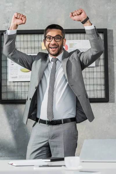 Alegre hombre de negocios triunfando y sonriendo a cámara en la oficina - foto de stock