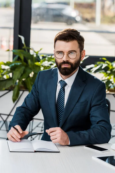 Confident buisnessman in eyeglasses sittting at workplace and looking at camera — Stock Photo