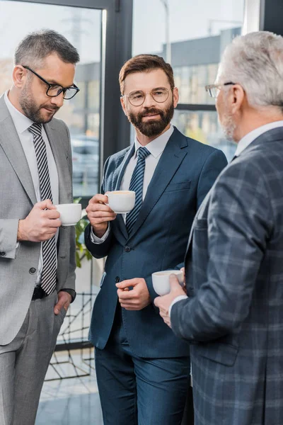 Бізнесмени тримають чашки кави і розмовляють в офісі — стокове фото