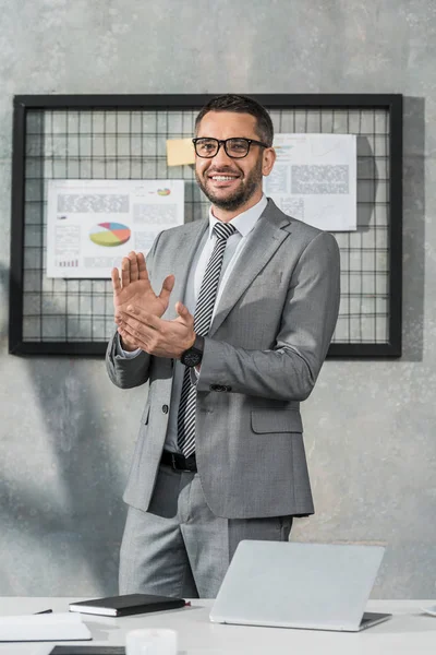 Gutaussehender, glücklicher Geschäftsmann, der im Büro applaudiert und in die Kamera lächelt — Stockfoto