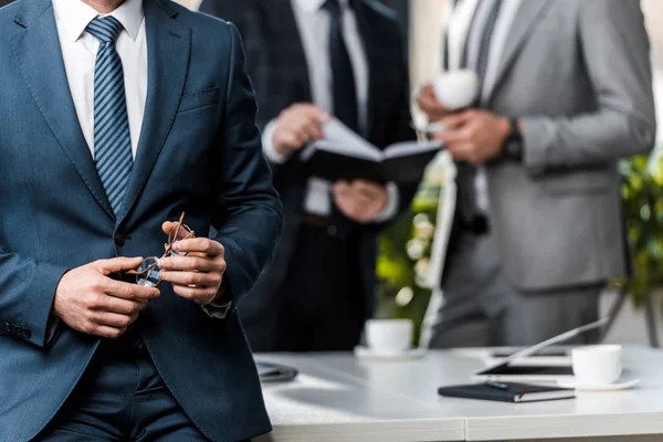 Cropped shot of businessman holding eyeglasses and colleagues working behind — Stock Photo