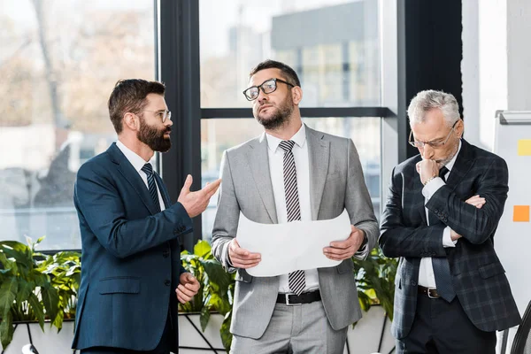 Serious professional businessmen discussing blueprint while standing in office — Stock Photo