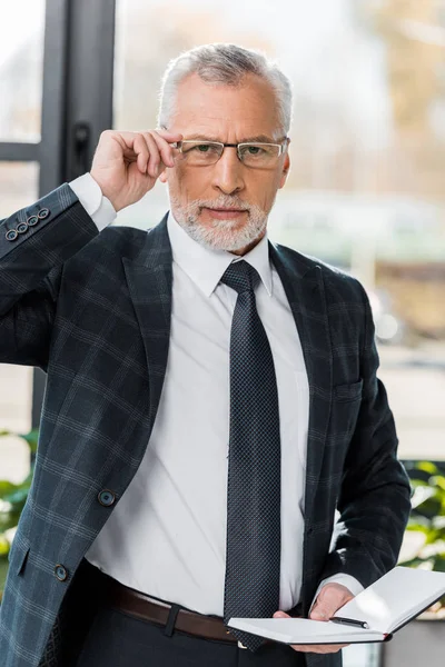 Selbstbewusster, reifer Geschäftsmann, der Brillen justiert und in die Kamera blickt — Stockfoto