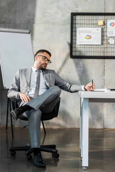 Нудний бізнесмен сидить на робочому місці і тримає ручку — стокове фото