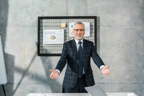 Fröhlicher reifer Geschäftsmann, der im Büro mit offenen Armen in die Kamera lächelt — Stockfoto