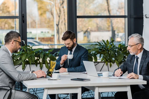 Tre uomini d'affari professionisti in abbigliamento formale che lavorano con dispositivi digitali in ufficio — Foto stock