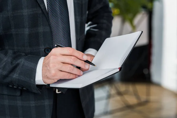 Close-up partial view of businessman in formal wear writing in notebook — Stock Photo