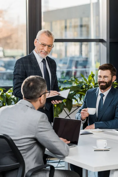 Smiling professional businessmen drinking coffee and working together in office — Stock Photo