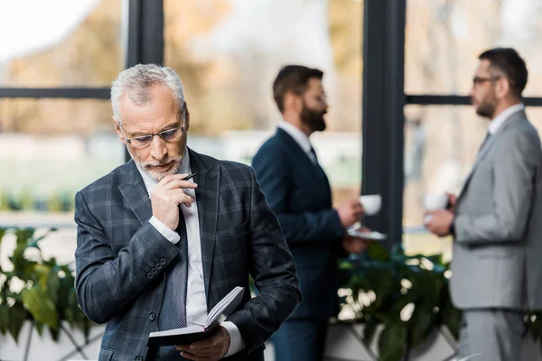Concentrated mature businessman holding pen and notepad in office — Stock Photo