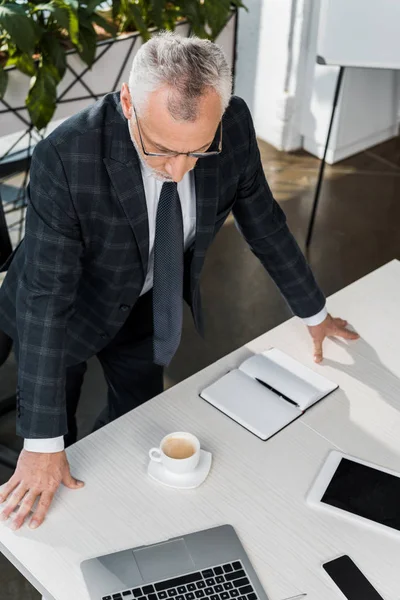 High angle view of mature buisnessman in eyeglasses and suit leaning at office table — Stock Photo