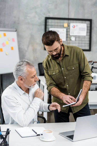 Focused businessmen looking at notepad and discussing work in office — Stock Photo