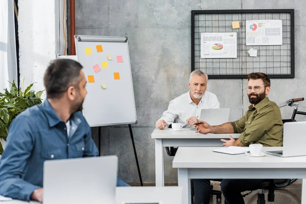 Hommes d'affaires professionnels utilisant des ordinateurs portables et se regardant tout en travaillant dans le bureau — Photo de stock