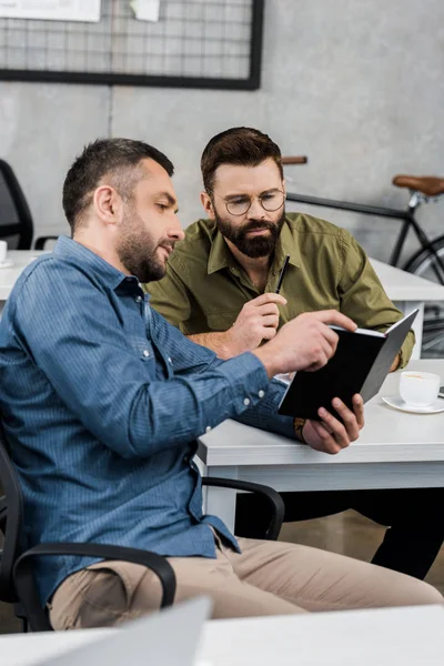 Geschäftsleute schauen auf Notizbuch und diskutieren Projekt im Büro — Stockfoto