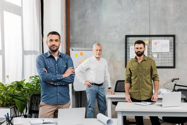 Guapos hombres de negocios de pie y mirando a la cámara en la oficina - foto de stock