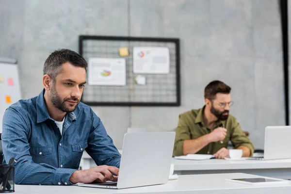 Dois homens de negócios bonitos trabalhando em laptops no escritório — Fotografia de Stock