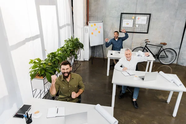 Высокий угол зрения счастливых красивых бизнесменов, показывающих да жест в офисе — стоковое фото