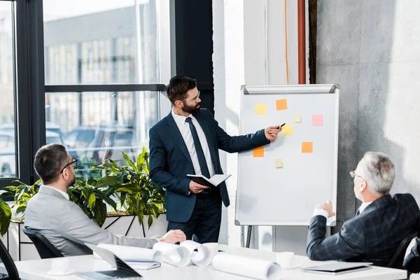 Handsome businessman pointing on flipchart during meeting in office — Stock Photo