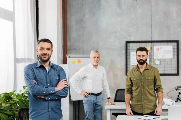 Three handsome businessmen standing and looking at camera in office — Stock Photo