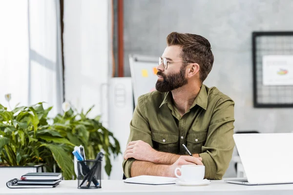 Side view of handsome bearded businessman in glasses looking away in office — Stock Photo
