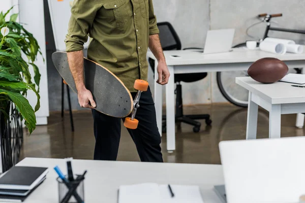 Immagine ritagliata di uomo d'affari in piedi con longboard in ufficio — Foto stock