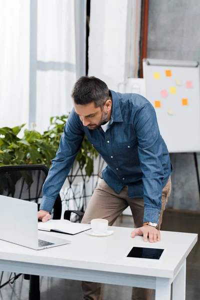 Schöner Geschäftsmann, der sich auf den Tisch lehnt und auf den Tisch im Büro schaut — Stockfoto