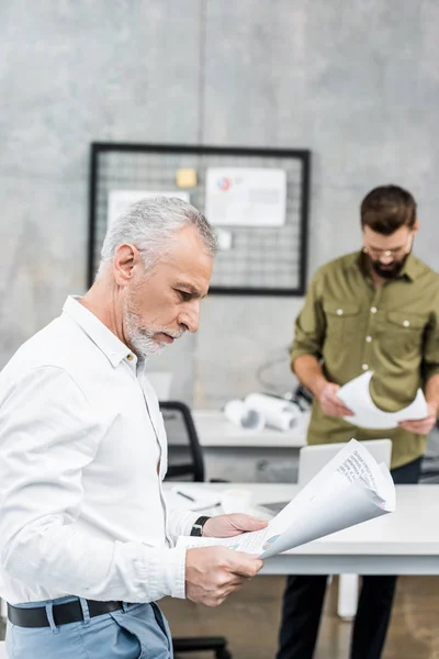 Gutaussehende Geschäftsleute betrachten Baupläne im Büro — Stockfoto