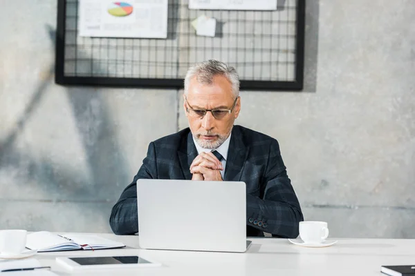 Nachdenklich gutaussehender Geschäftsmann mittleren Alters schaut im Büro auf Laptop — Stockfoto