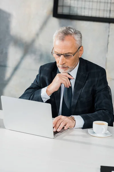 Высокий угол зрения застенчивого красивого бизнесмена средних лет, смотрящего на ноутбук в офисе — стоковое фото