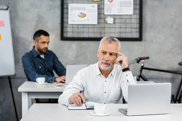 Cher beau homme d'affaires assis à table et regardant loin dans le bureau — Photo de stock