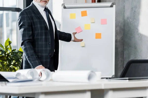 Imagen recortada de hombre de negocios de mediana edad señalando en el rotafolio en la oficina - foto de stock