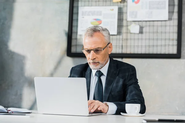 Pensativo guapo mediana edad hombre de negocios en gafas de trabajo en el ordenador portátil en la oficina - foto de stock