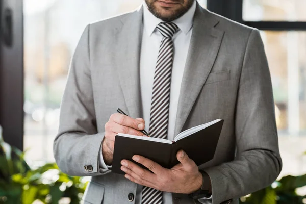 Image recadrée de l'homme d'affaires en costume écrit quelque chose à portable dans le bureau — Photo de stock