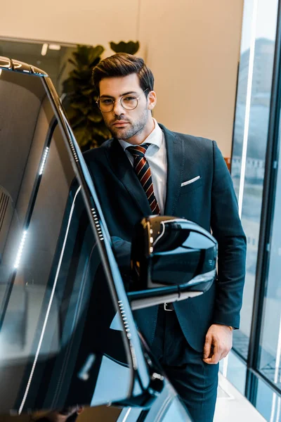 Hombre de negocios en gafas de vista mirando a la cámara cerca de coche - foto de stock