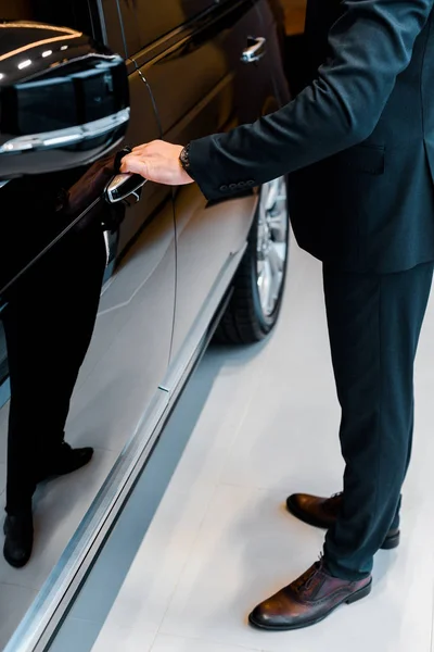 Imagen recortada de hombre de negocios en traje abriendo la puerta de automóvil negro - foto de stock