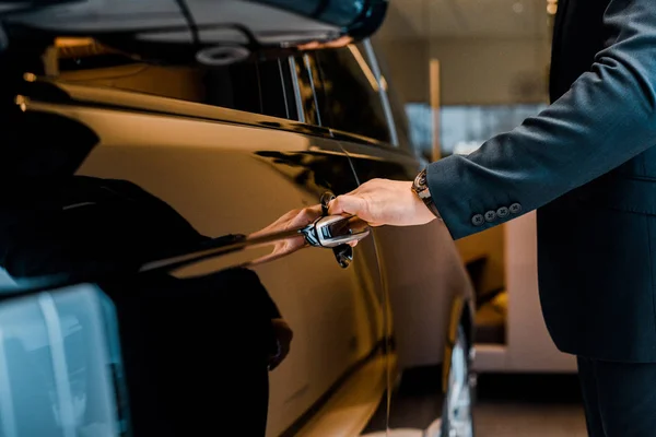 Imagen recortada de hombre de negocios en traje abriendo la puerta de automóvil negro - foto de stock