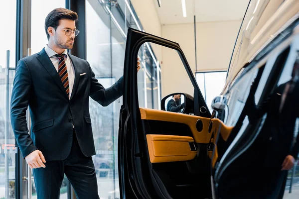 Homme d'affaires confiant dans les lunettes ouvrant la porte de l'automobile noire — Photo de stock